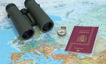 Spanish passport with binoculars and compass on a map, representing Spain immigration reforms and visa travel in 2025