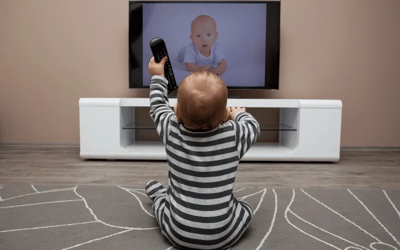 Baby sitting on floor watching television and holding remote control