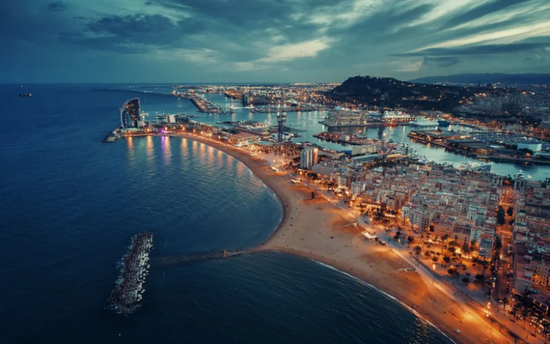 Aerial night view of Barcelona coastline with city lights and harbor
