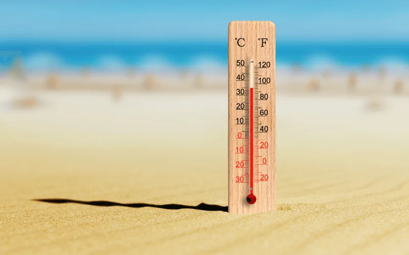 thermometer showing high temperature on sandy beach under summer sun