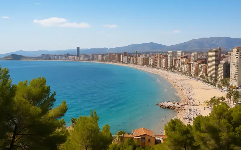 Panoramic view of a Mediterranean beach city in Spain with golden sand, blue sea, and mountains in the background
