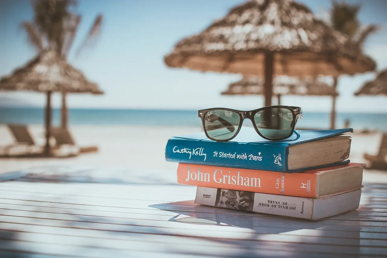 Books, sunglasses on table with bach and sunshades in background