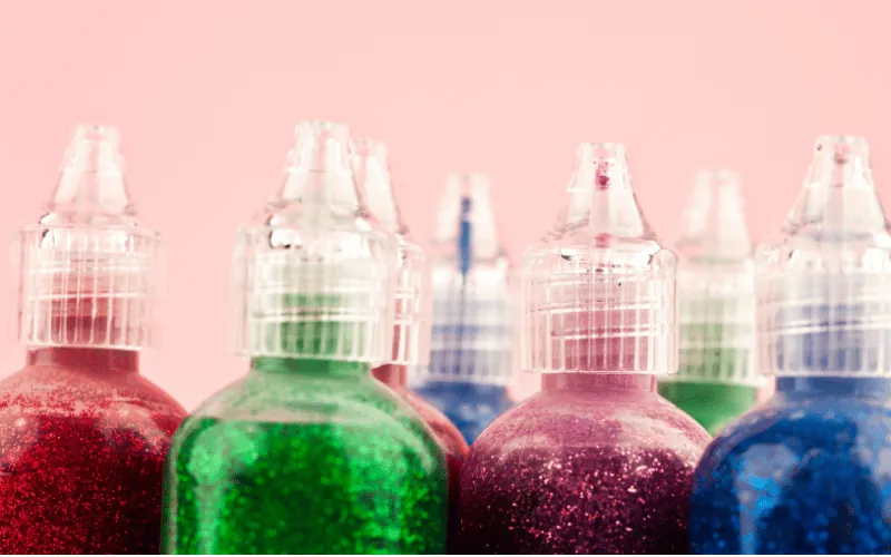 Colorful glitter glue bottles for arts and crafts on pink background