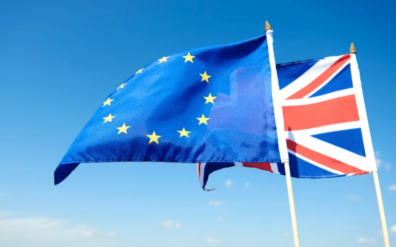uropean Union and United Kingdom flags waving together against clear blue sky
