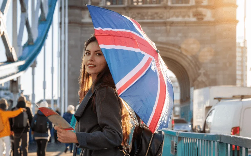 Woman holding Union Jack umbrella on Tower Bridge in London at sunset