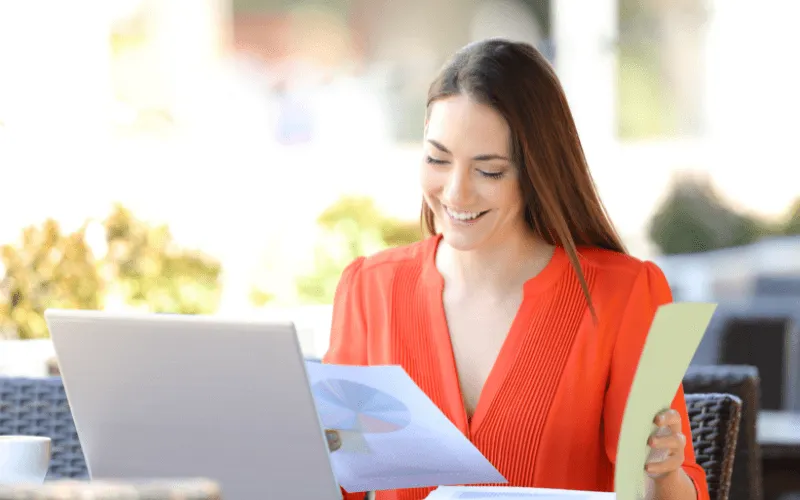 Smiling businesswoman working on laptop with financial documents outdoors