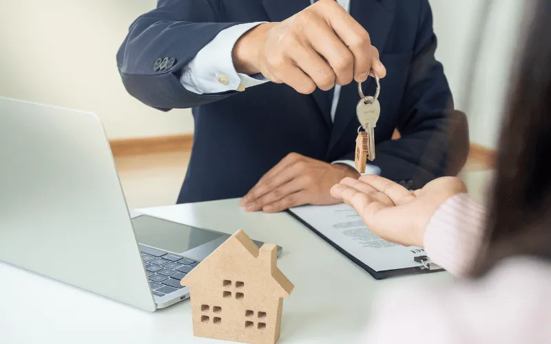 Real estate agent handing over house keys to new property owner with paperwork on the desk