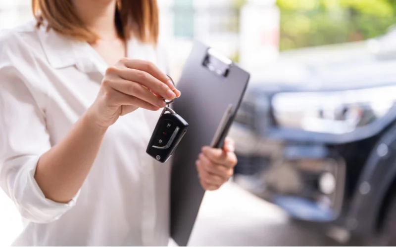 Woman handing over car keys during rental process with clipboard in hand