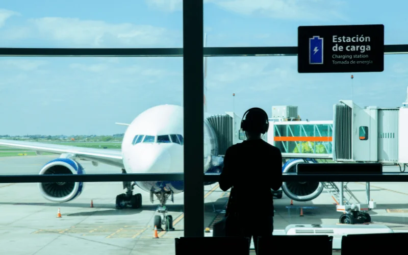 Traveler at airport gate near charging station with airplane on runway
