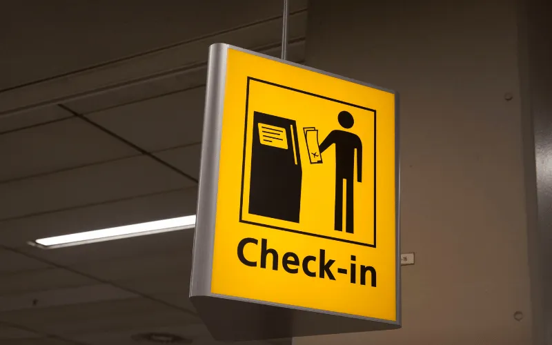 ellow check-in sign at airport showing passenger with boarding pass at kiosk