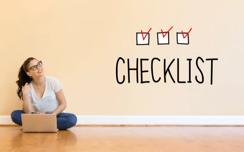 Smiling woman sitting with laptop next to completed checklist on wall