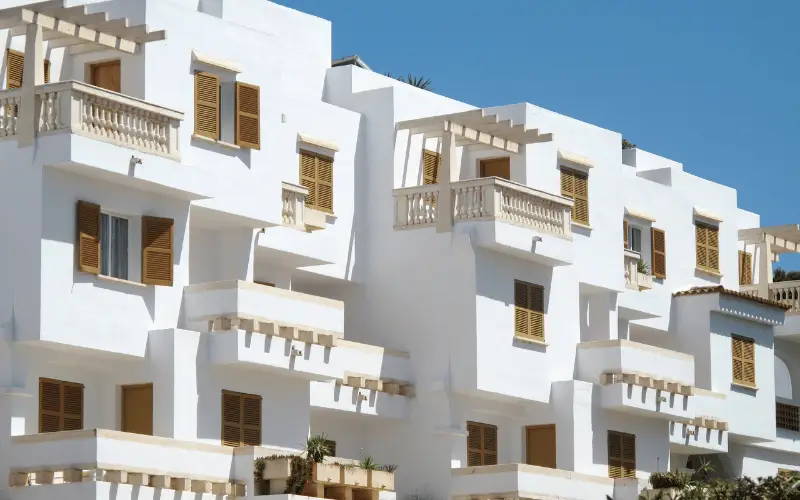 White Mediterranean-style apartment building with wooden shutters under clear blue sky