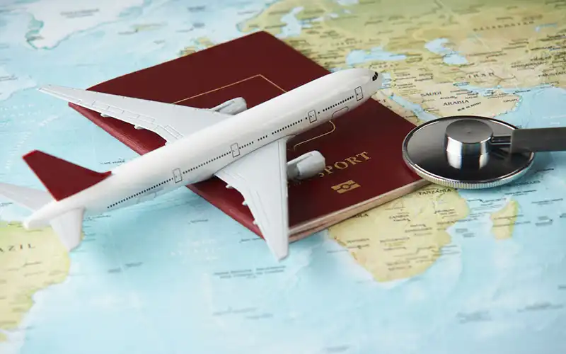 Toy airplane, red passport, and stethoscope on a world map – symbolising travel and healthcare coverage in 2025