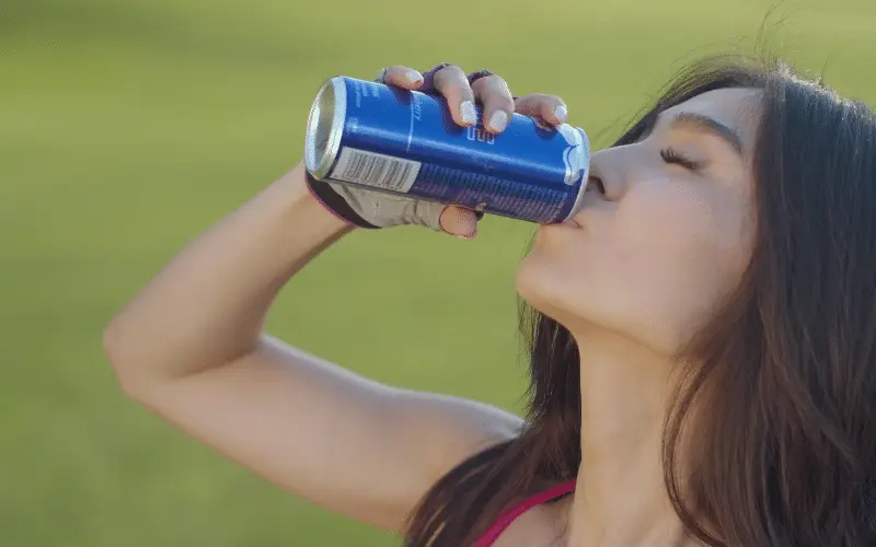 Woman drinking energy drink from a can after workout outdoors for hydration and fitness boost