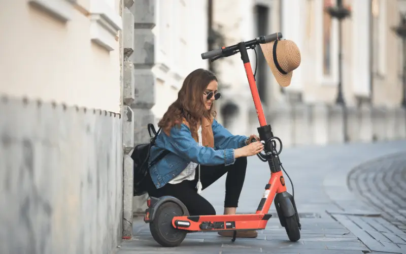 Young woman adjusting electric scooter while sitting on a city street