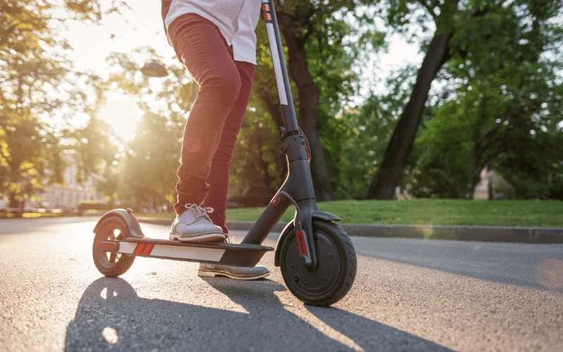 Person riding electric scooter through sunny park path