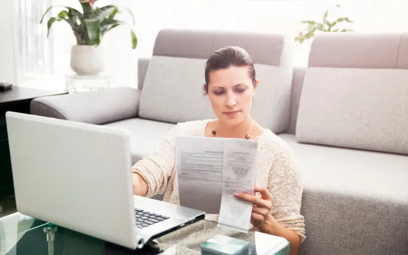 Woman checking her taxes in front of her laptop while sitting on the floor