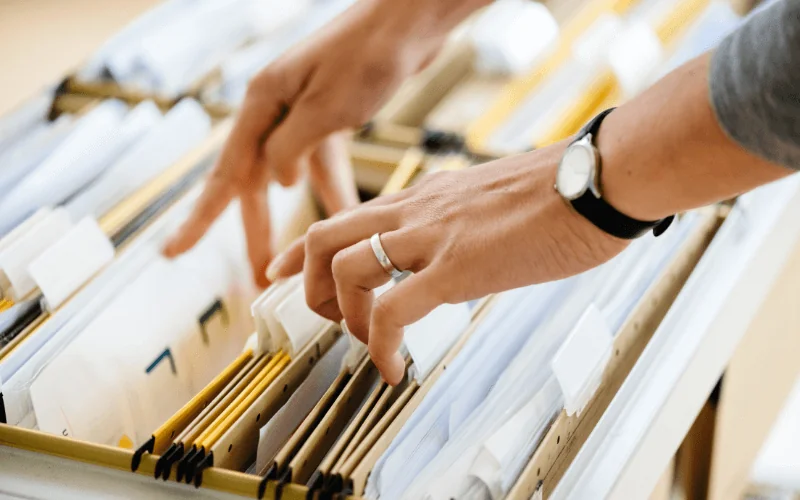 Person searching through paperwork in organized office filing cabinet