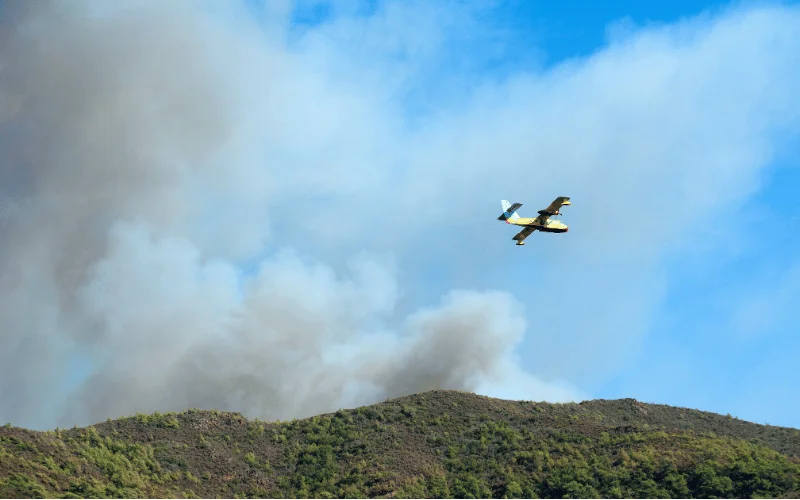 Water bomber plane fights forest wildfire in Spain with smoke rising over mountain ridge