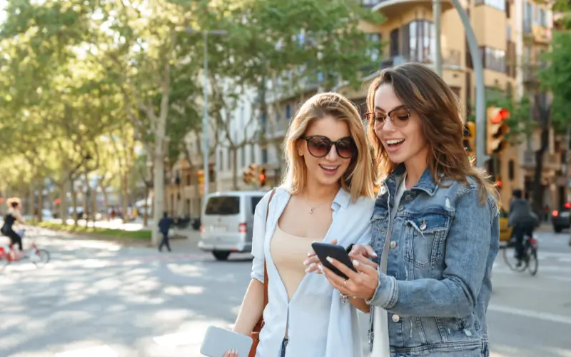 Two young women by the roadside looking at something on their mobile phone