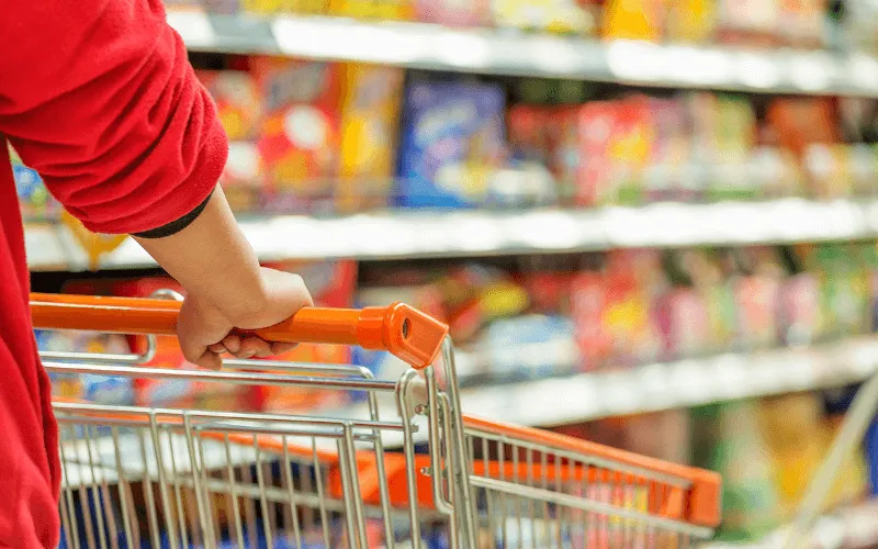 Person pushing shopping trolley in a supermarket aisle filled with food products in Spain