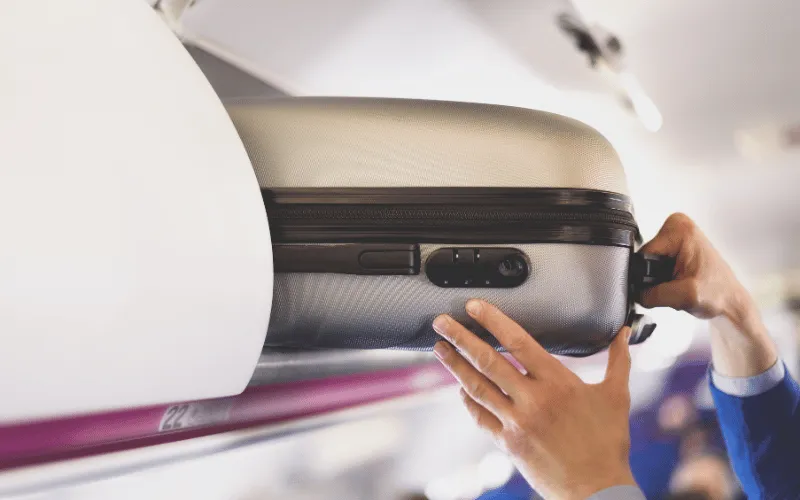 Passenger placing carry-on suitcase in airplane overhead compartment