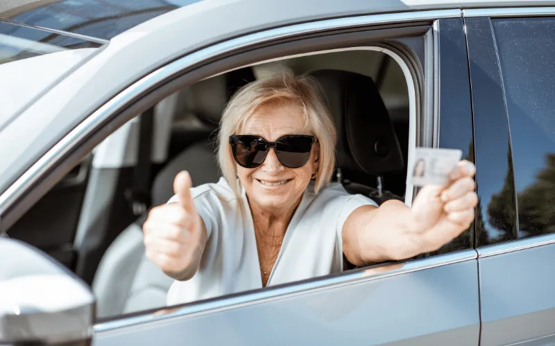 Smiling senior woman showing her driver’s license while sitting in a car