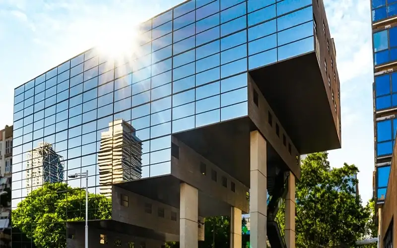 Modern glass building reflecting city skyline with sunlight and trees