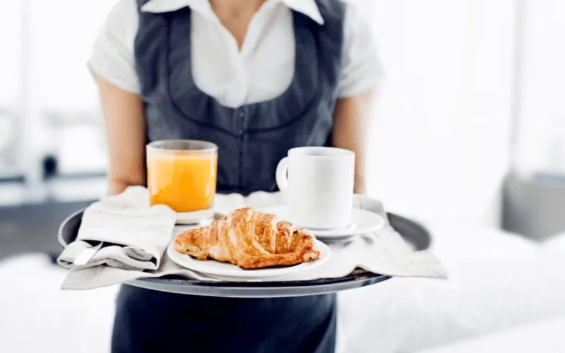 Hotel staff serving breakfast with coffee, juice, and croissant on a tray in a Spanish hotel room