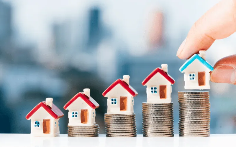 Miniature houses on stacked coins symbolizing property investment and rising housing costs
