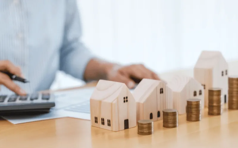 Person using calculator with wooden house models and stacked coins representing property tax planning