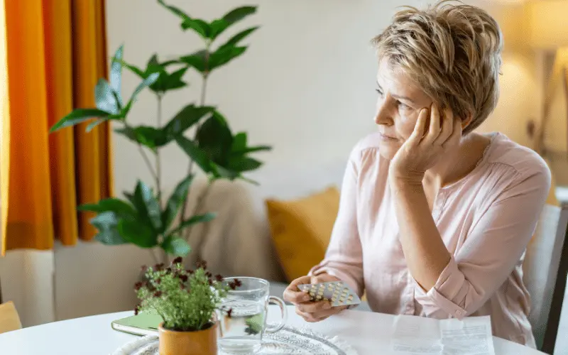 Middle-aged woman holding medication and experiencing menopause symptoms at home