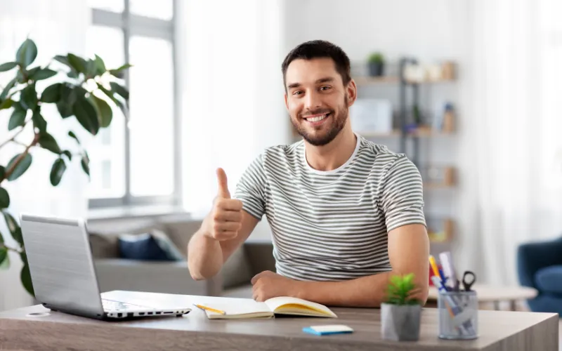 Man giving thumbs up while working on laptop from home office