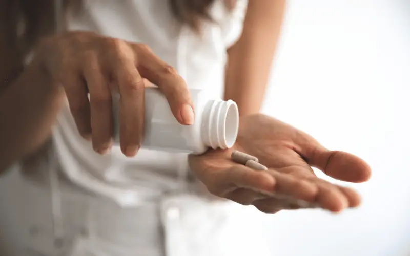 Woman taking magnesium supplement capsules from bottle for daily health support, energy, and muscle recovery