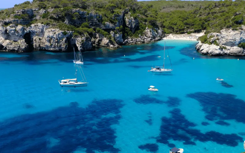 Sailboats anchored in turquoise waters of a hidden cove in Menorca