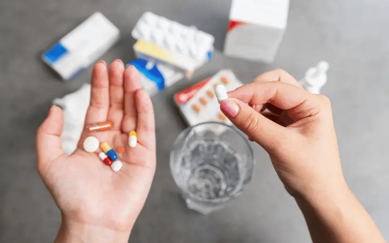 Person holding multiple pills and tablets with water and medication boxes on table