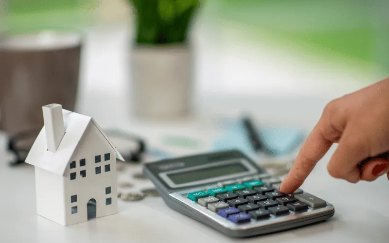 Person using calculator next to small house model for mortgage planning