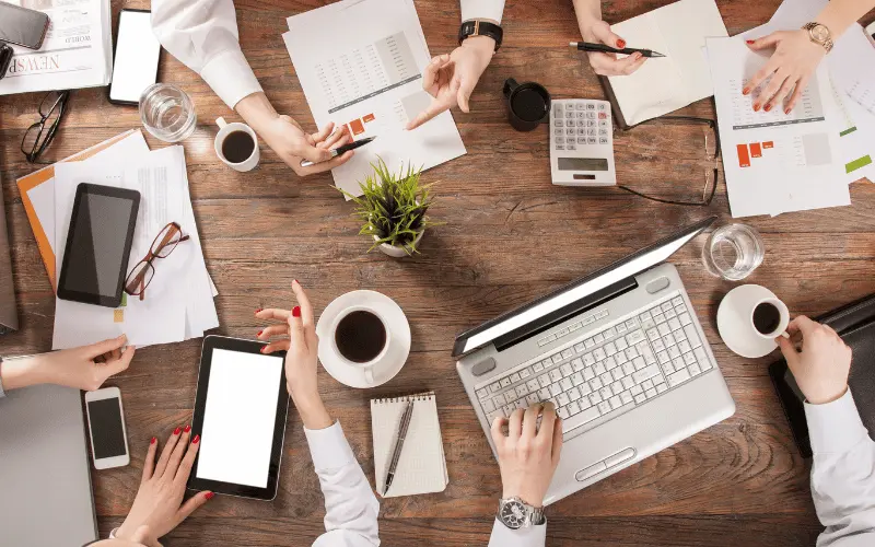 Team meeting with business documents, coffee, and devices on office table