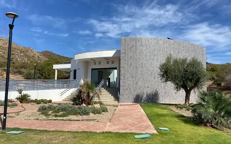 Modern building with curved facade and landscaped garden in a hilly area under blue sky