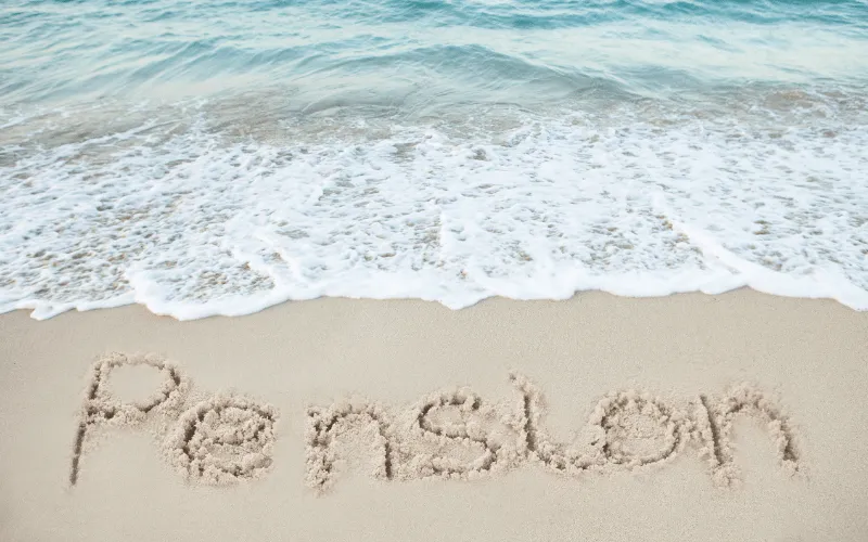 The word pension written in sand on beach with ocean waves in background