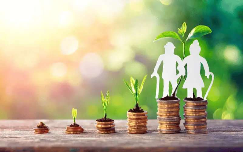 Stacks of coins with growing plants and paper cutouts of elderly couple symbolizing retirement savings and financial growth