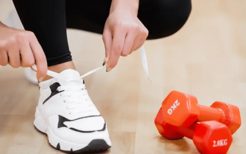 Woman tying sneakers before indoor workout with dumbbells for fitness and weight loss