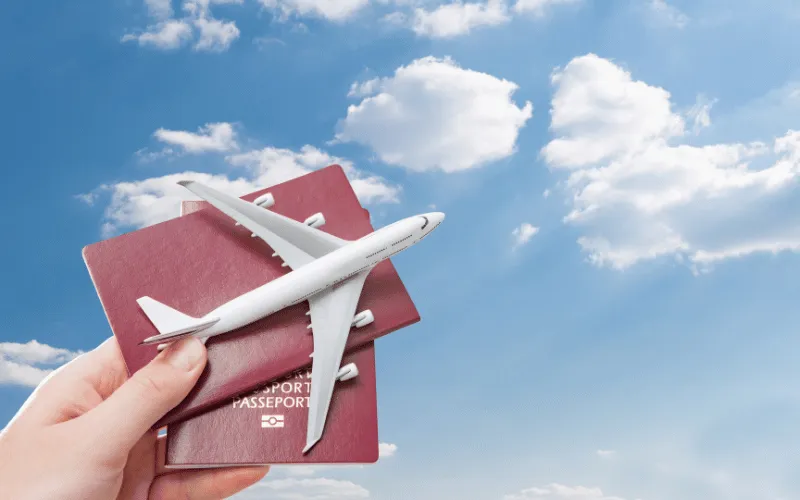 Hand holding passports with toy airplane against blue sky with clouds