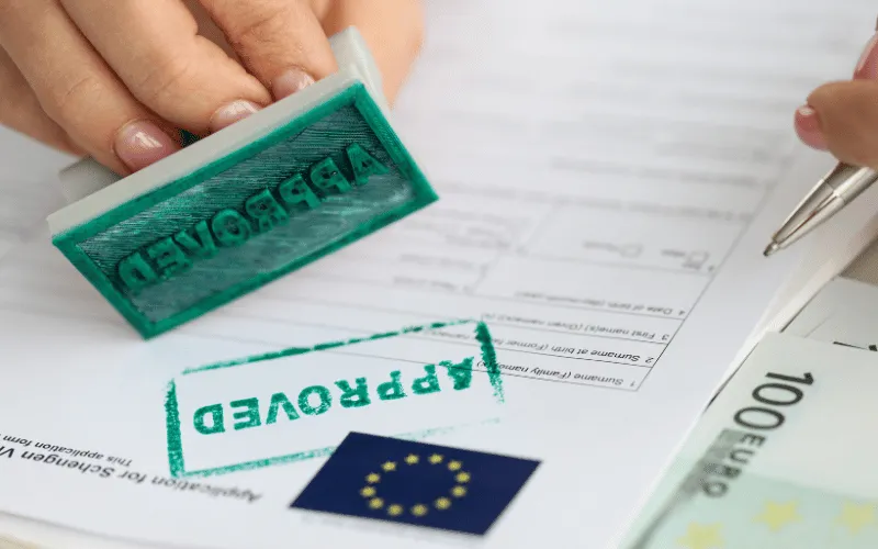 Approved stamp on Schengen visa application form with EU flag and euro banknotes