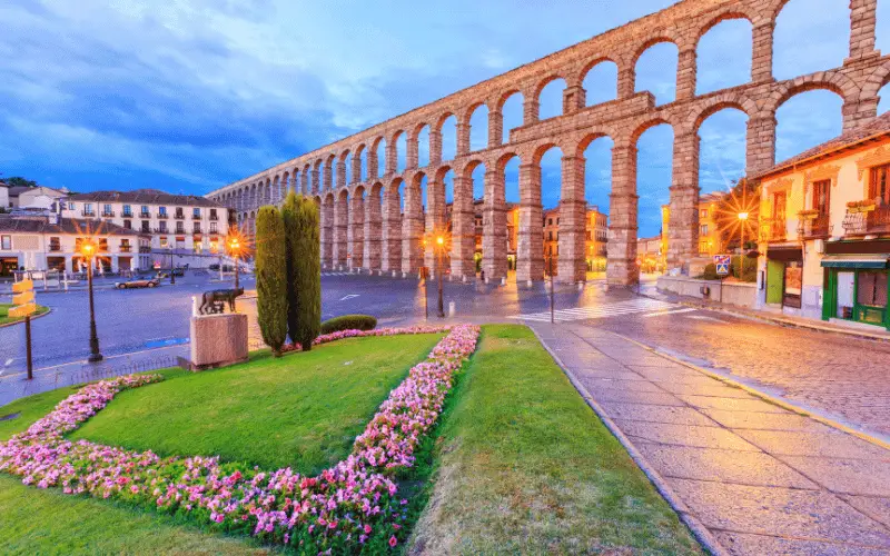 Historic Roman aqueduct in Segovia Spain with flowers and old town architecture at sunset