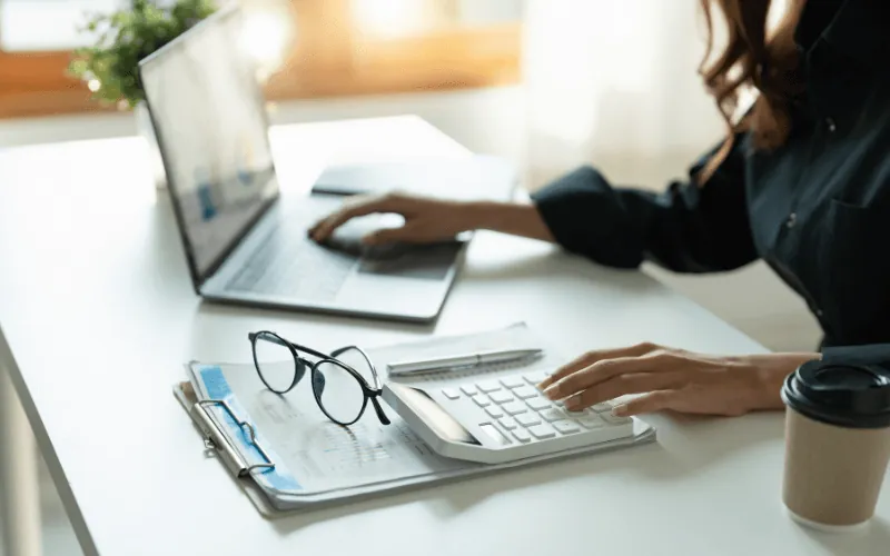 Self-employed person calculating finances with laptop and documents on desk