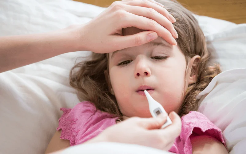 Sick child with thermometer being cared for at home during illness