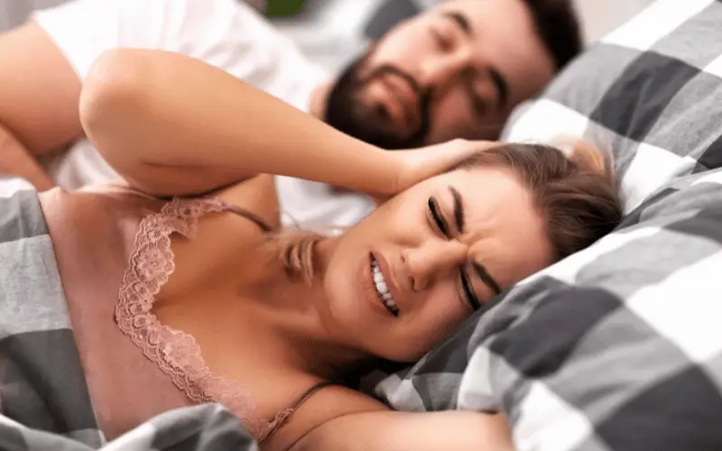 Woman covering ears in bed while partner snores loudly during sleep