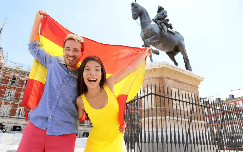 Happy international couple celebrating in Spain with flag at Plaza Mayor in Madrid