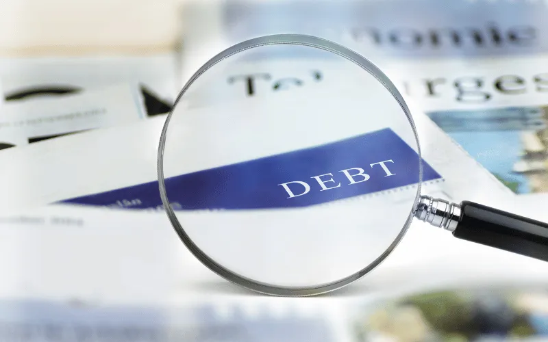 Magnifying glass highlighting the word debt in a newspaper article